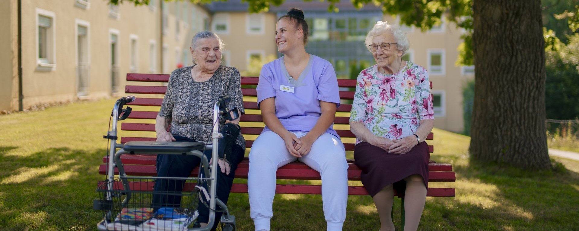 eine Pflegerin die sich um zwei aeltere Damen kuemmert im Garten 