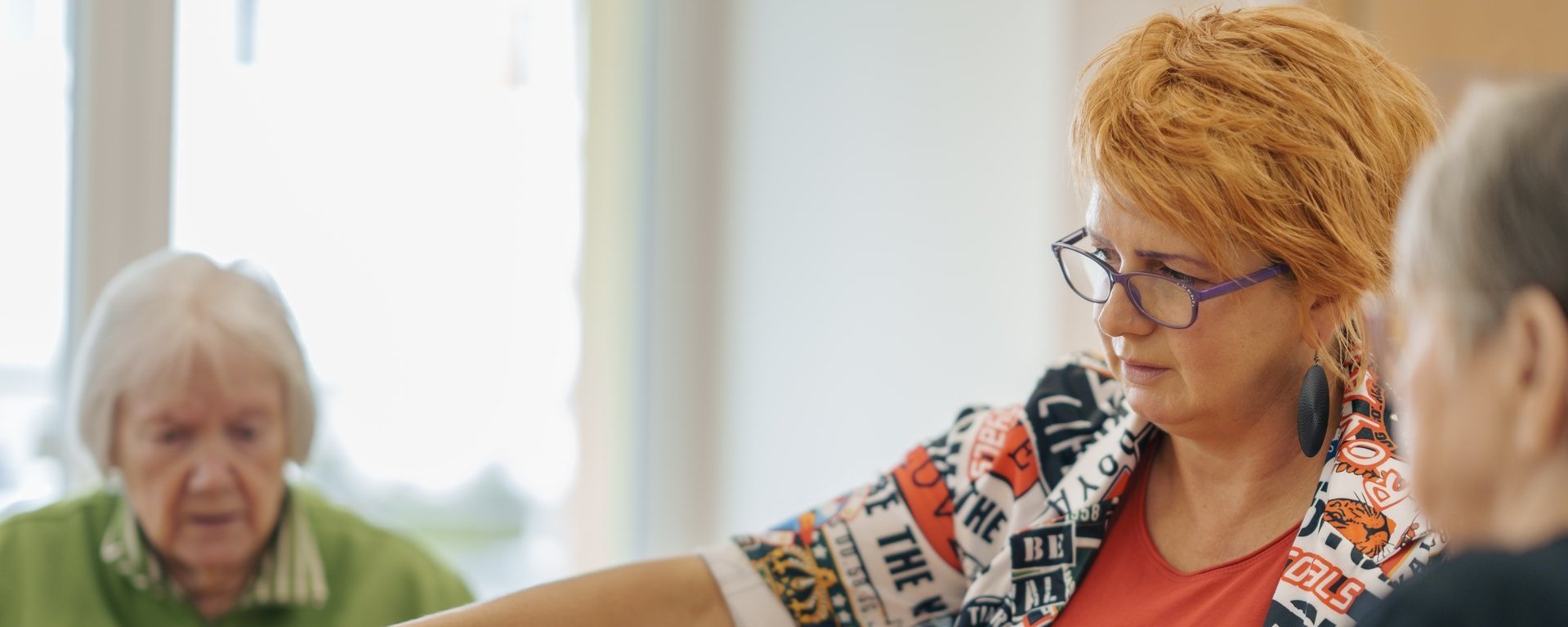 Zwei Bewohnerinnen und eine Pflegekraft spielen zusammen ein Brettspiel  